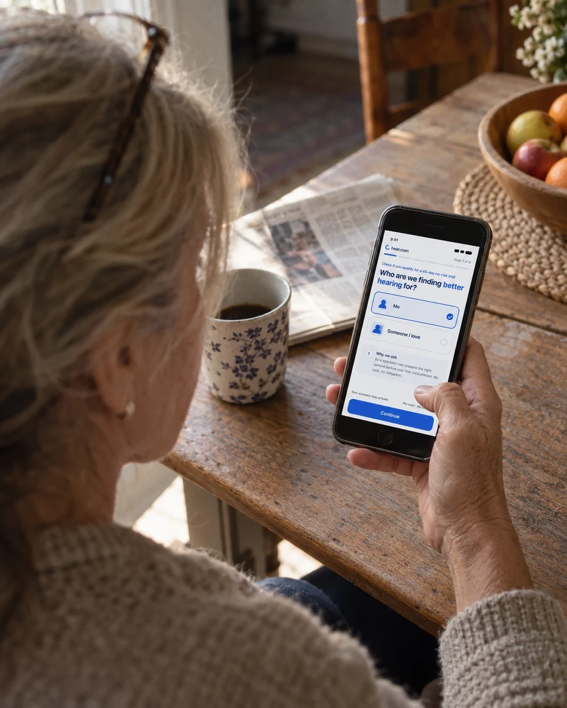 A woman at her kitchen table answering the hear.com questionnaire on her phone