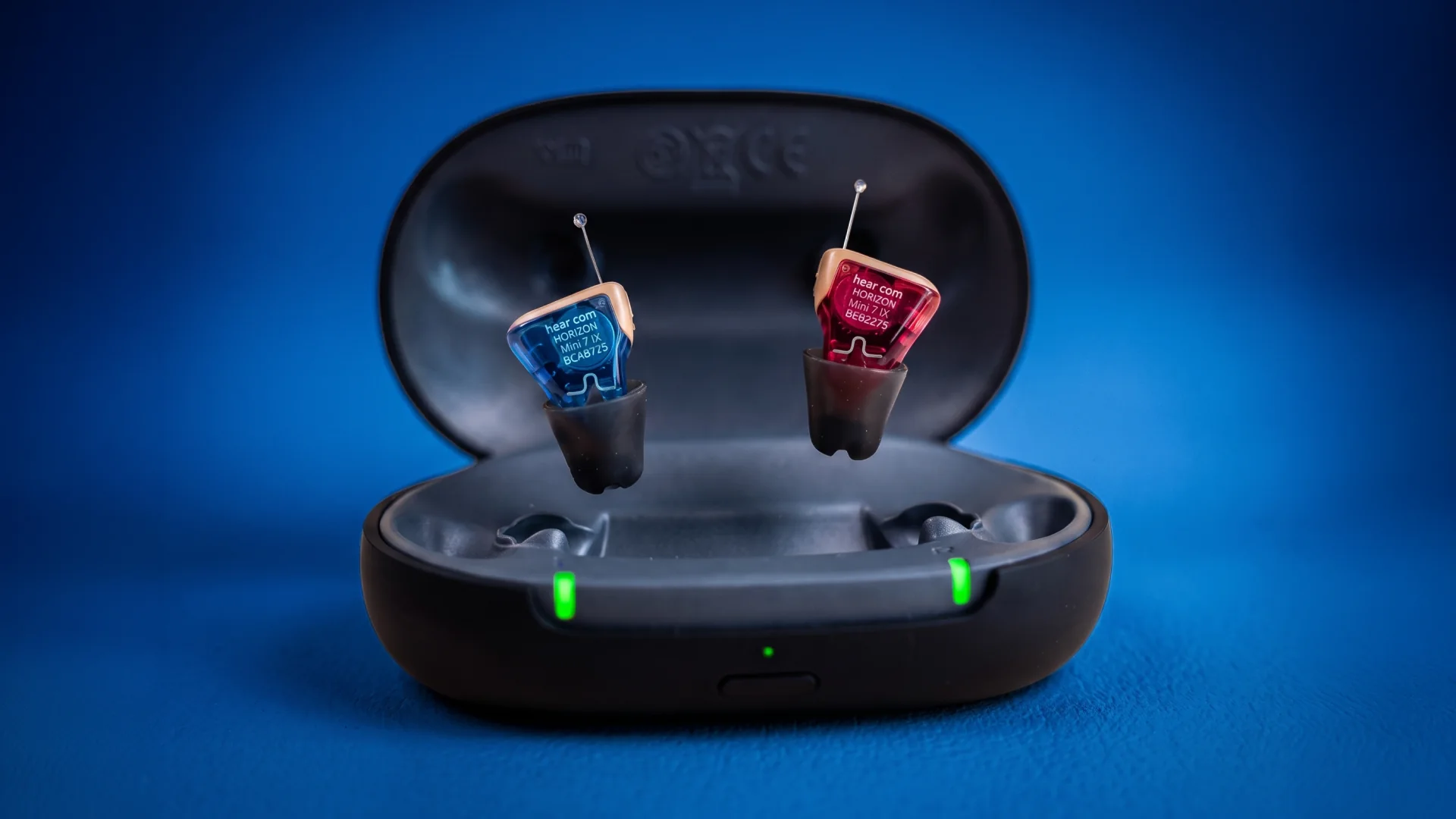 Blue and red IX hearing aids floating above an open charging case