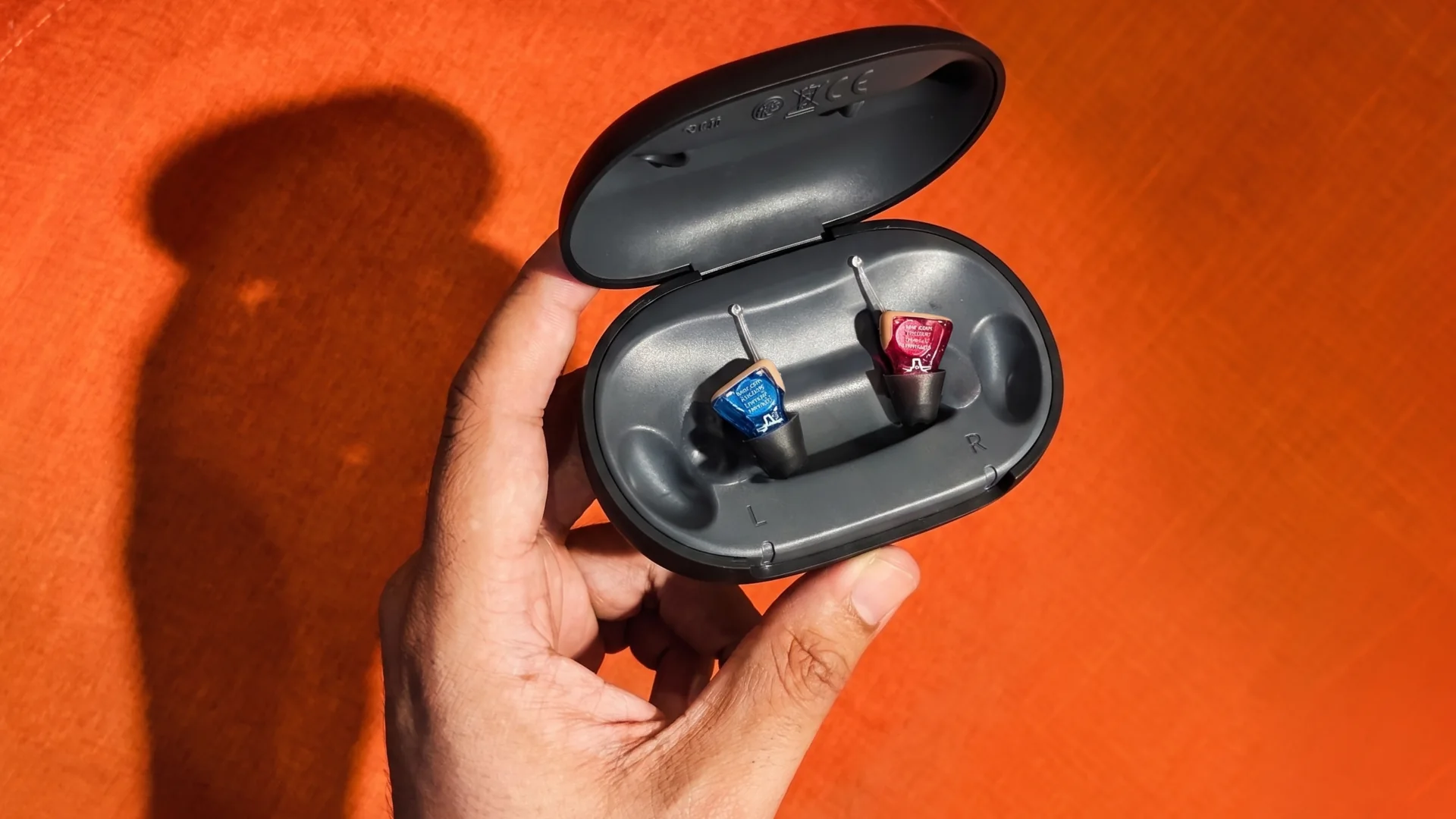 Two IX hearing aids in their charging case, held against an orange wall